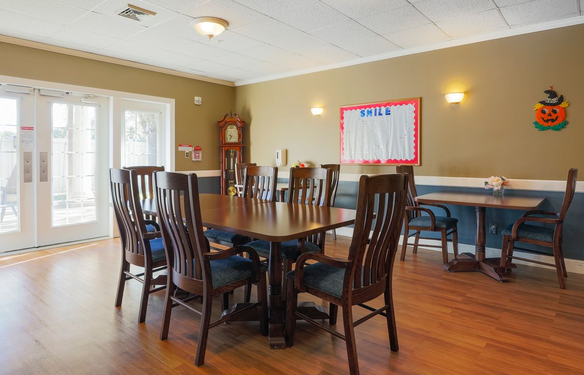 A spacious meeting room with a large conference table surrounded by chairs, featuring a bulletin board and clock on the walls.