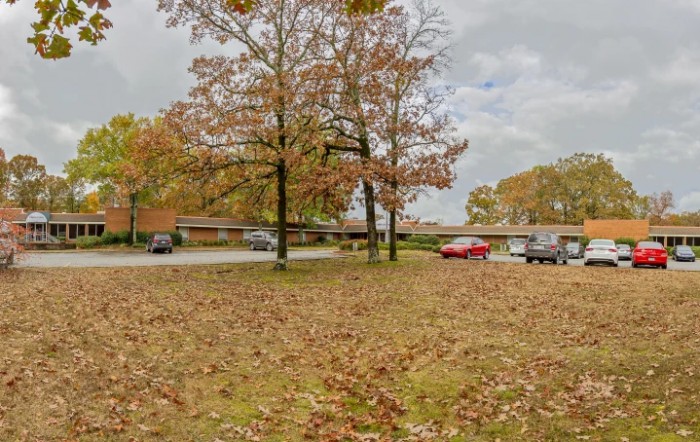 A suburban scene in autumn with trees shedding their leaves and cars parked along the street.