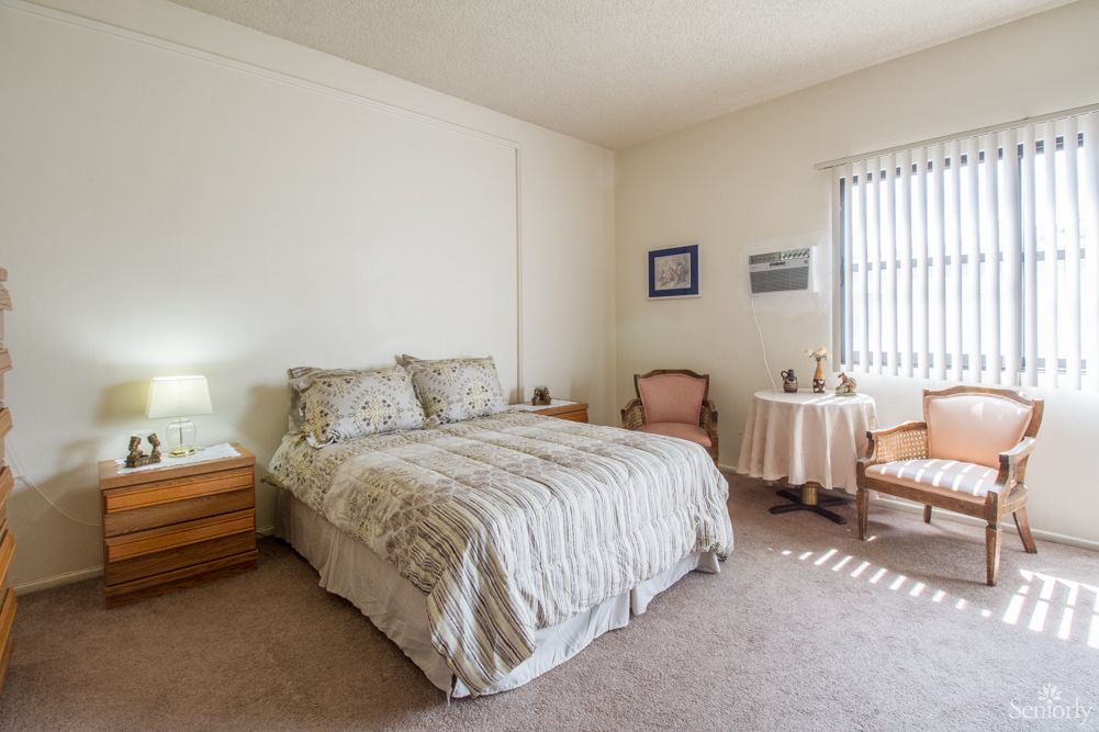 A cozy bedroom with a large bed, two chairs around a small table, and simple decor.