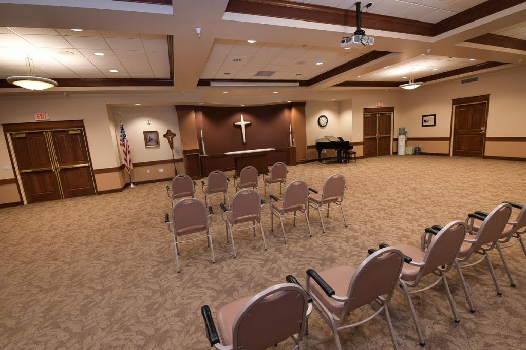A small chapel with rows of chairs facing an altar, featuring a cross on the wall.