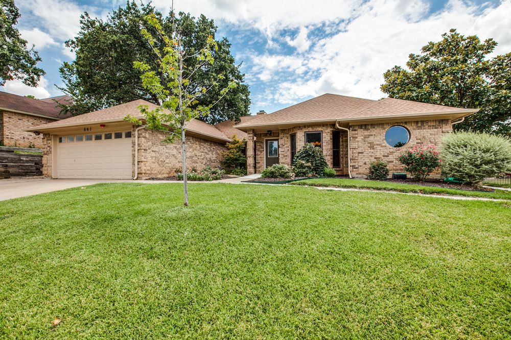 A suburban brick house with a well-maintained lawn and surrounding trees.