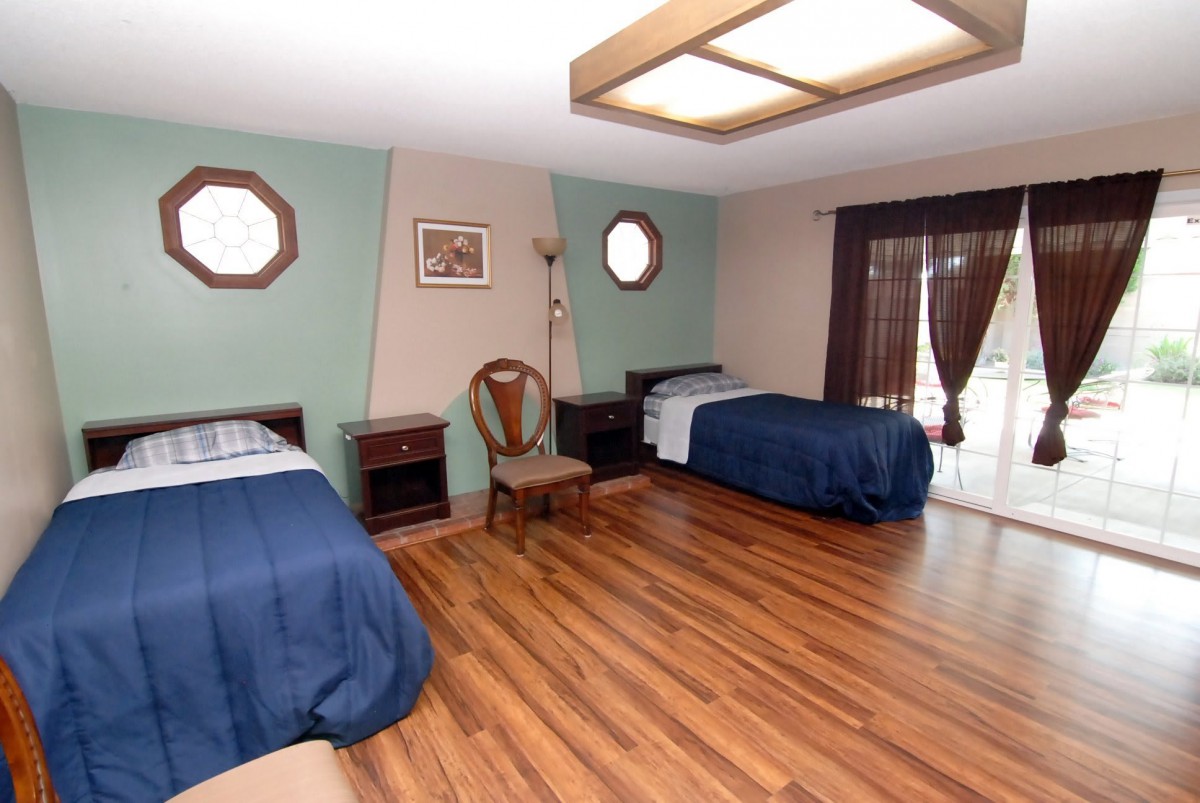A spacious bedroom with two single beds, wooden flooring, and decorative windows allowing natural light.