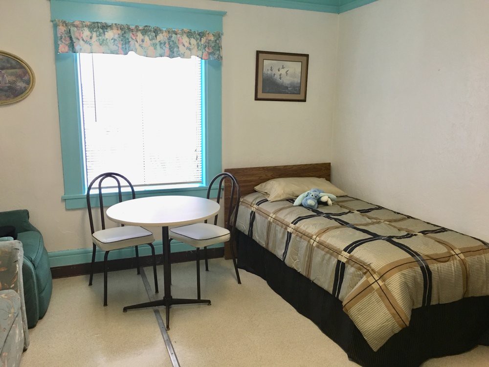 A cozy bedroom with a single bed, a small round table, and two chairs by the window.
