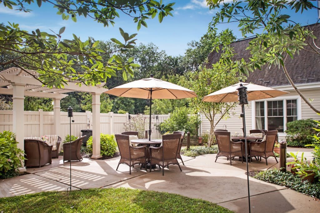 A sunny patio area with outdoor tables, chairs, and umbrellas surrounded by greenery.