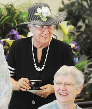 Two elderly women enjoying a tea party, one wearing a decorative hat and holding a teacup.