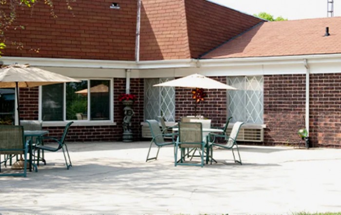 A sunny patio area with tables, chairs, and umbrellas in front of a brick building.