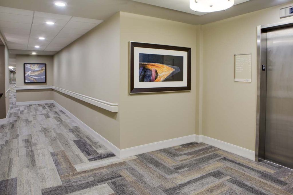 A well-lit hallway featuring a piece of framed artwork on the wall and patterned flooring.