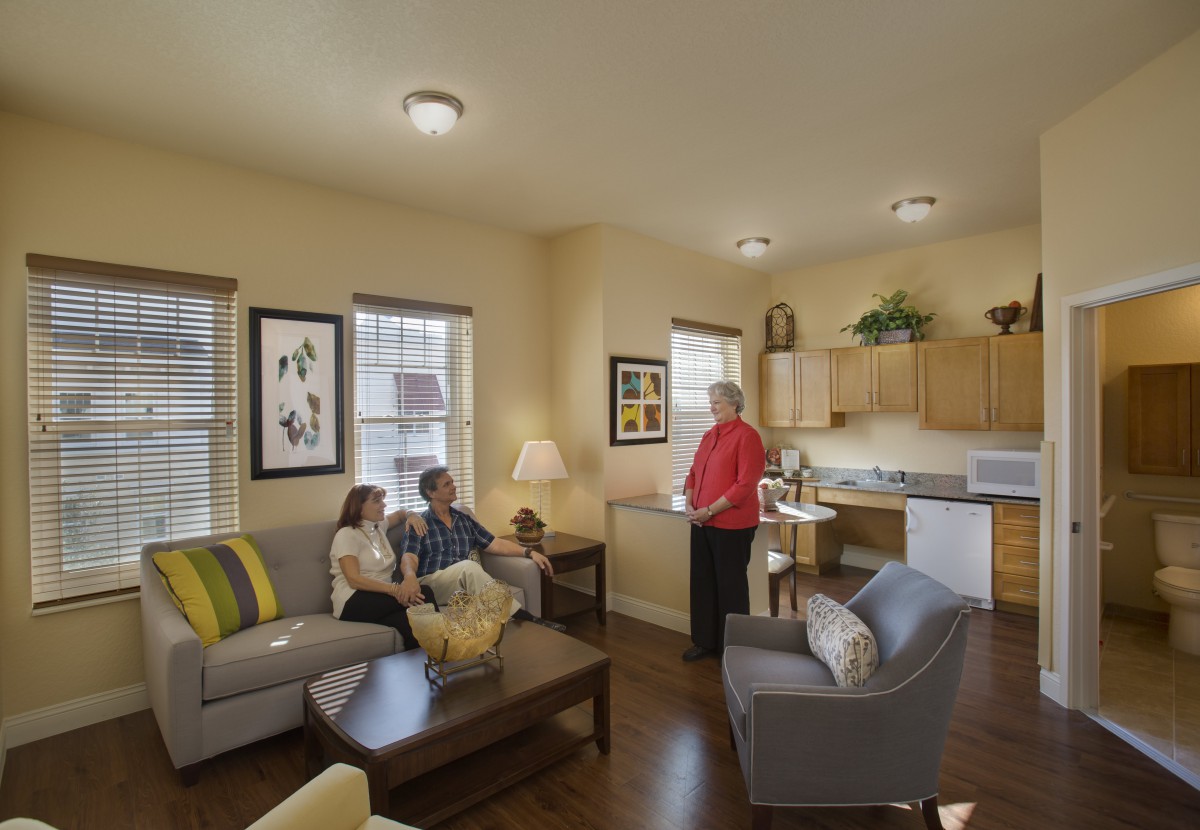 Three people in a cozy living area with an open kitchen layout.