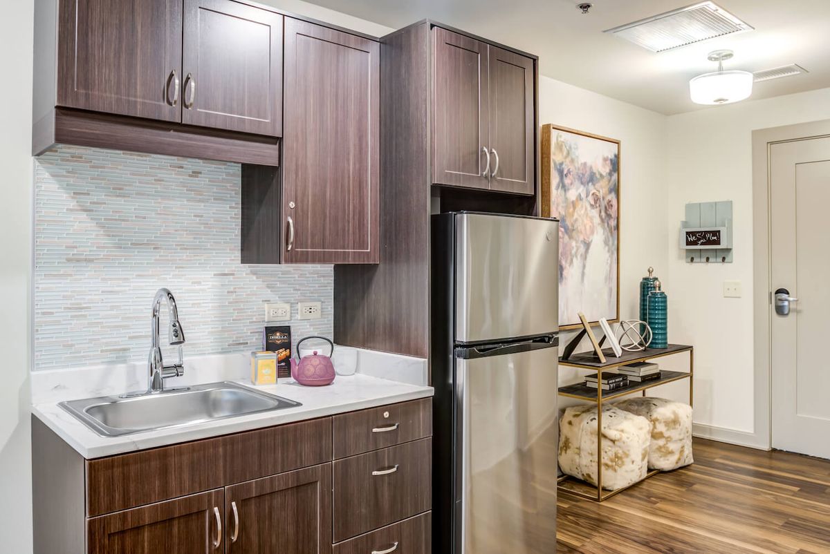 A modern kitchen interior featuring dark wood cabinets, a stainless steel refrigerator, and a small sink area.