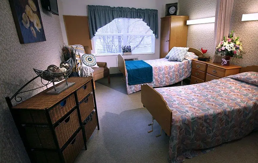 A cozy bedroom featuring two neatly made beds, decorated with floral and solid color linens, alongside a window with curtains.