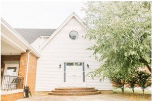 A charming white house with a gabled roof and brick steps leading to the entrance, flanked by trees.