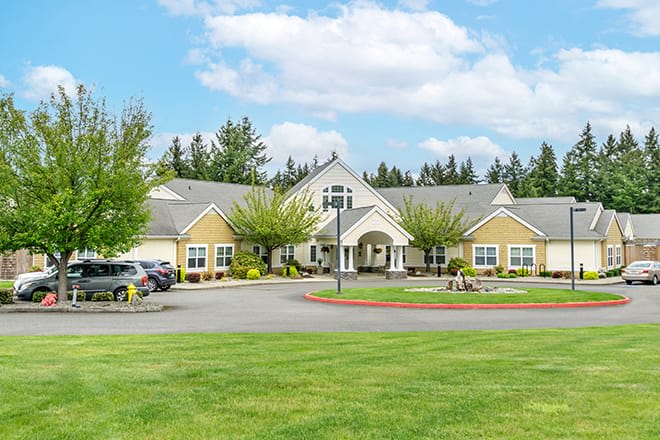 A picturesque residential building surrounded by a lush green lawn and trees, with a clear blue sky above.