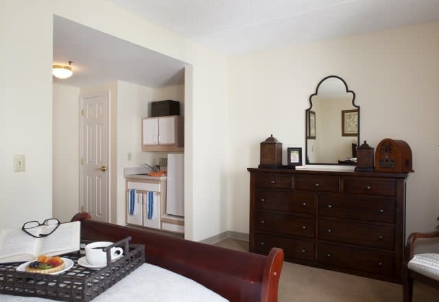 A cozy bedroom featuring a dark wooden dresser with an ornate mirror and neatly arranged decor items.