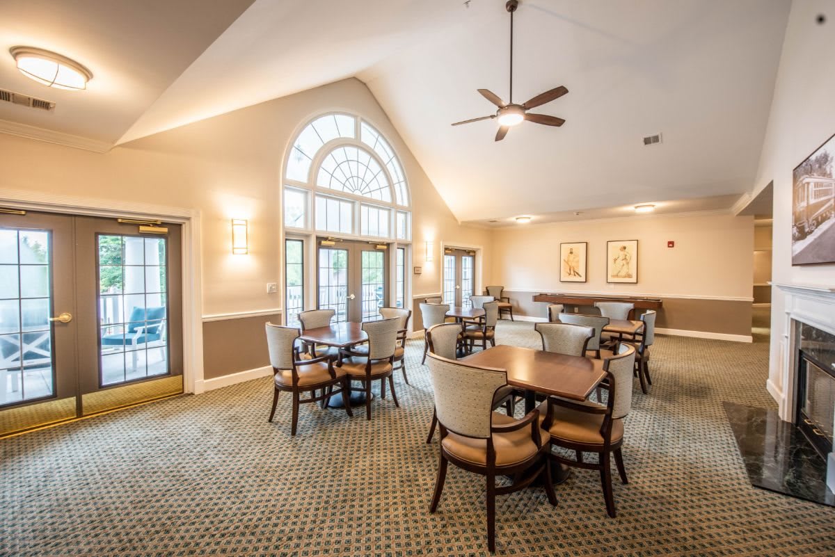 A spacious, well-lit dining area with multiple tables and chairs, featuring large windows and a ceiling fan.