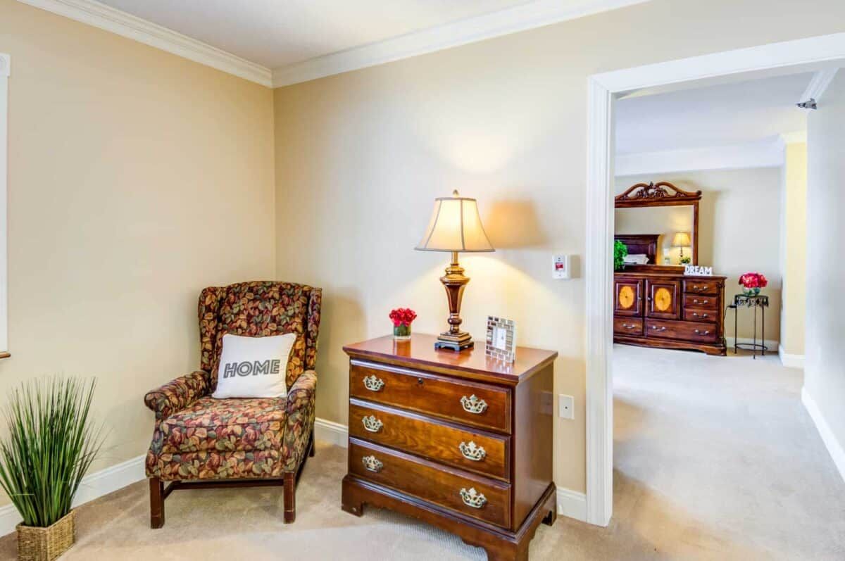 A cozy living space with a patterned armchair, wooden dresser, and lamp.