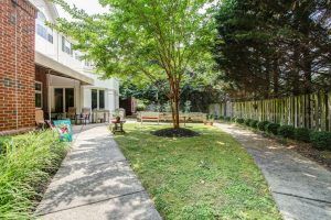 A peaceful backyard with a tree, grassy area, patio, and outdoor furniture.