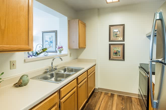A clean and tidy kitchen with wooden cabinets, a double sink, and wood flooring.