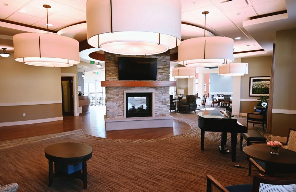 A spacious and modern lounge area featuring a central fireplace, stylish lighting, and a grand piano.