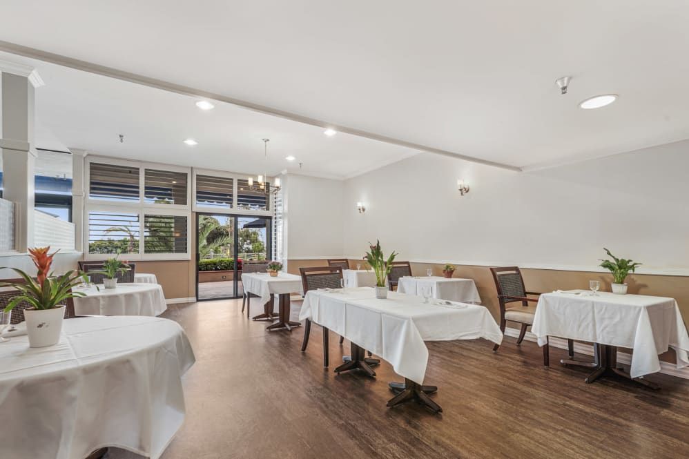A spacious restaurant interior with neatly arranged tables covered in white tablecloths.