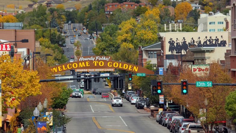 A scenic view of a city street in Golden, Colorado with autumn foliage and a welcoming sign.
