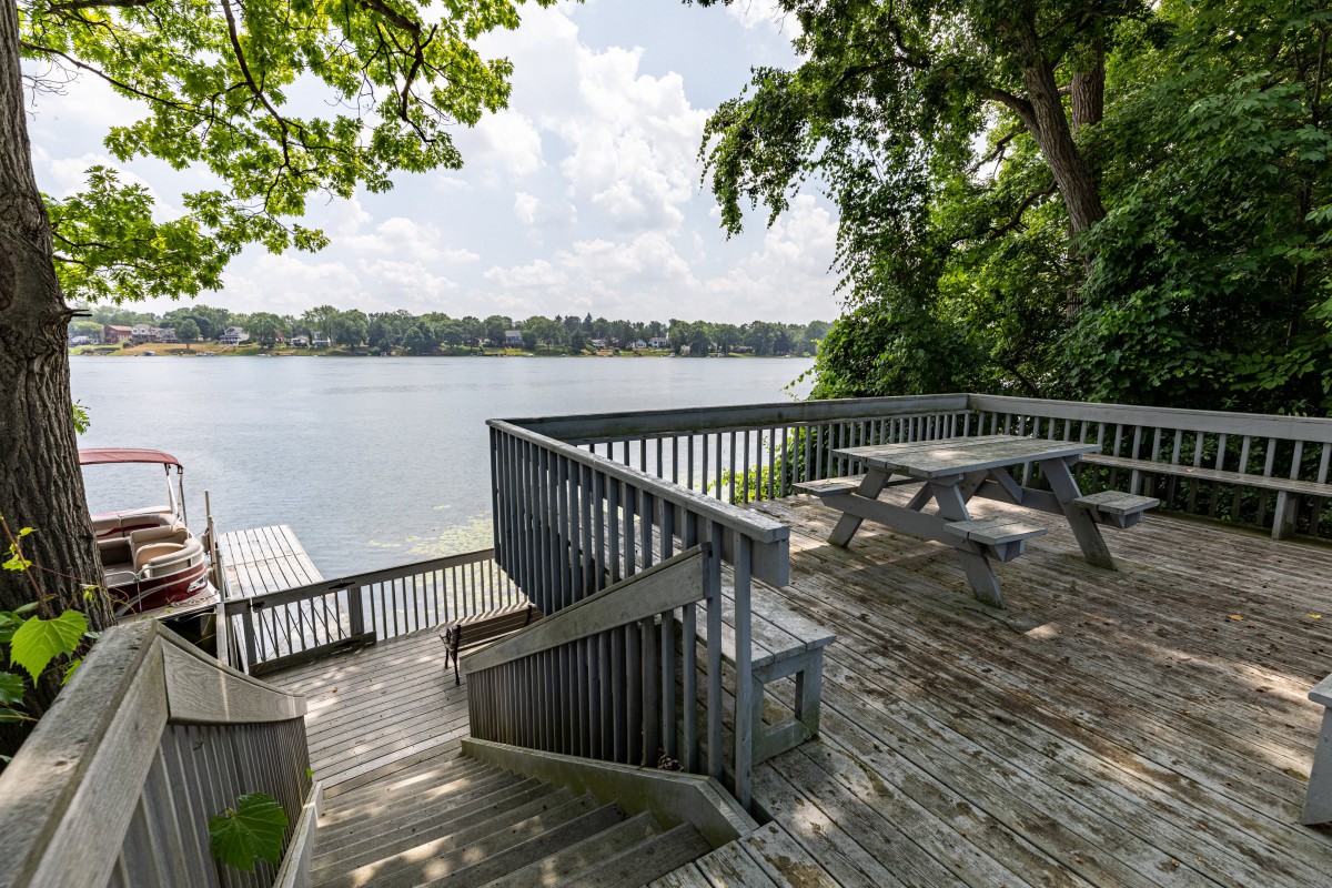 A peaceful wooden deck overlooking a serene lake with a picnic table and surrounded by lush trees.