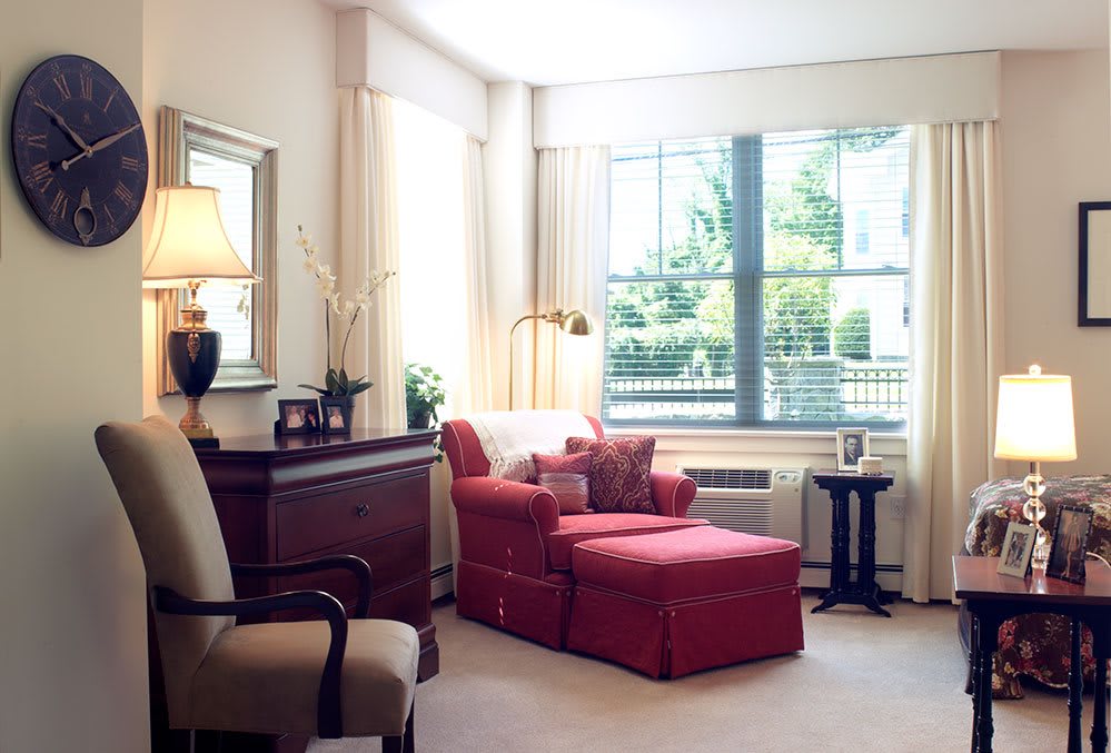 A cozy living room with a red armchair and ottoman near a large window.