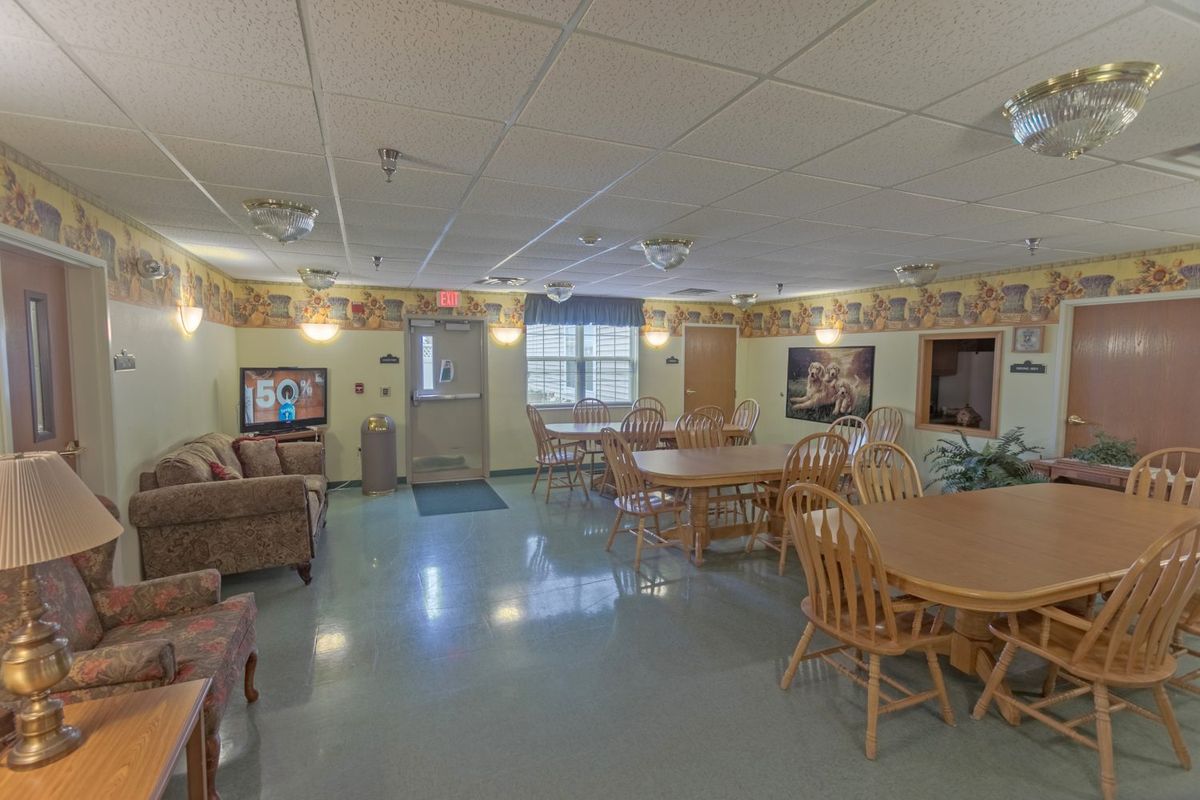 A well-lit community dining and living area with wooden tables and chairs, decorated walls, and a comfortable seating arrangement.