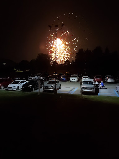 A stunning display of fireworks illuminates the night sky over a crowded parking lot.