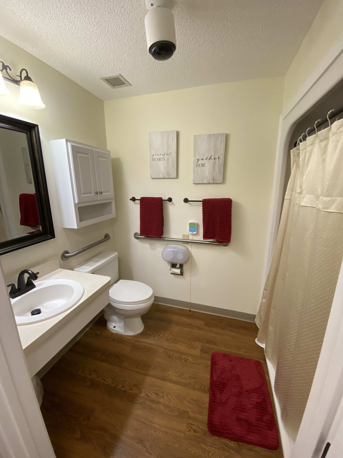 A well-organized bathroom featuring a sink, toilet, and shower with red towels and wooden flooring.