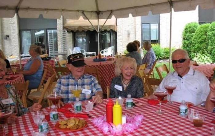 A group of seniors enjoying a picnic under a tent with checkered tablecloth.