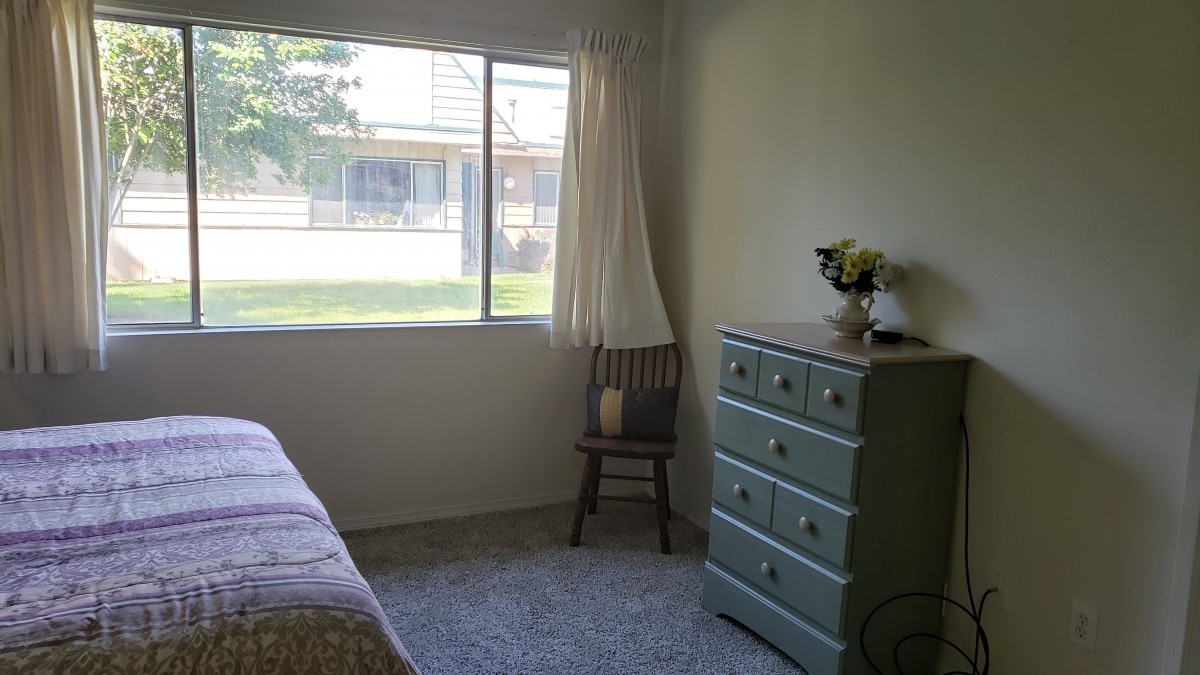 A cozy bedroom with a window, dresser, and chair.