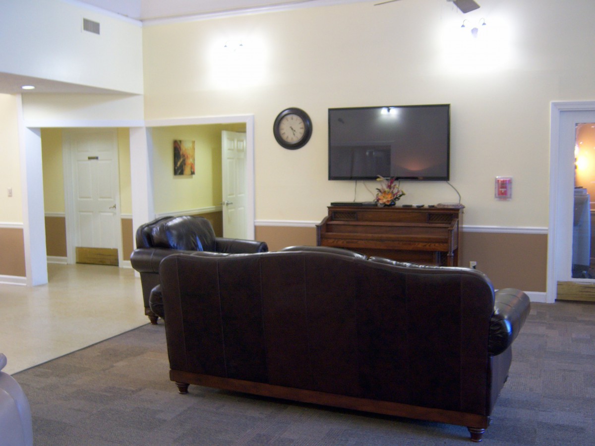 A cozy living room featuring a sofa set, wall-mounted television, and a piano.