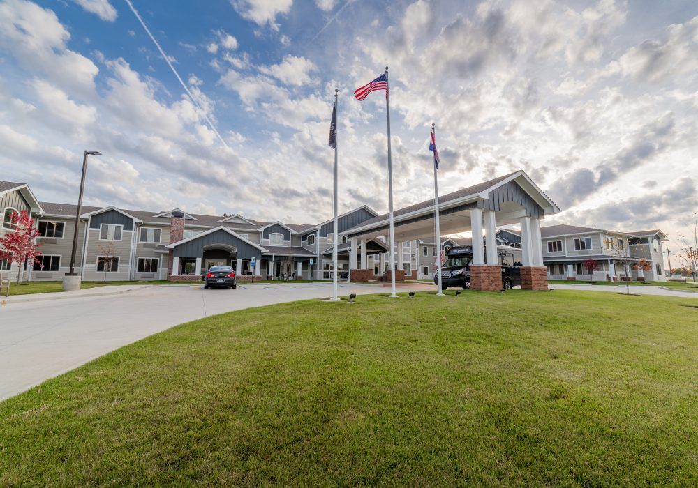 A large building with several flags out front, surrounded by a well-maintained lawn and set against a cloudy sky.