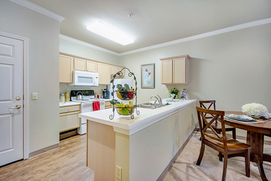 A modern kitchen with a central island and bar stools, featuring white cabinets and various appliances.