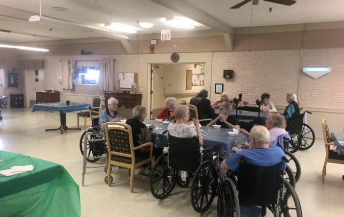 A group of elderly people in wheelchairs gathered indoors at a nursing home.