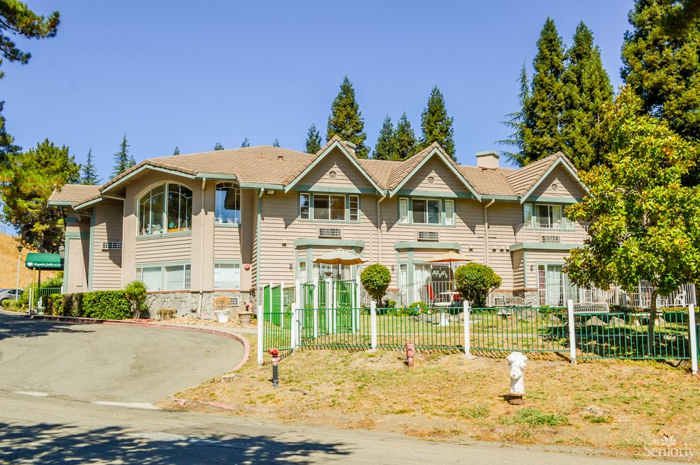 A large suburban house with a fenced yard and surrounding trees.