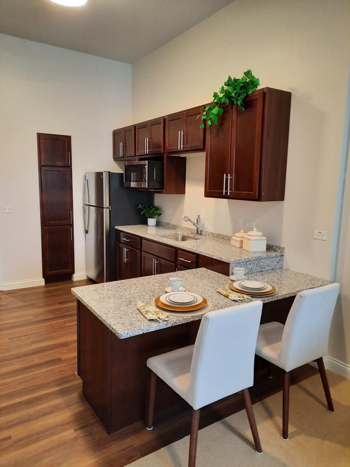A modern kitchen with wood cabinetry, stainless steel appliances, and a marble countertop with bar seating.