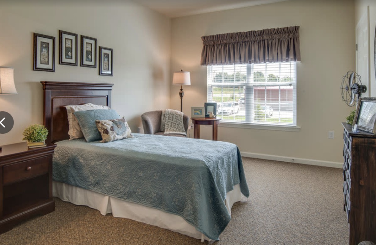 A cozy bedroom with a single bed, a chair by the window, and soft lighting from a floor lamp.