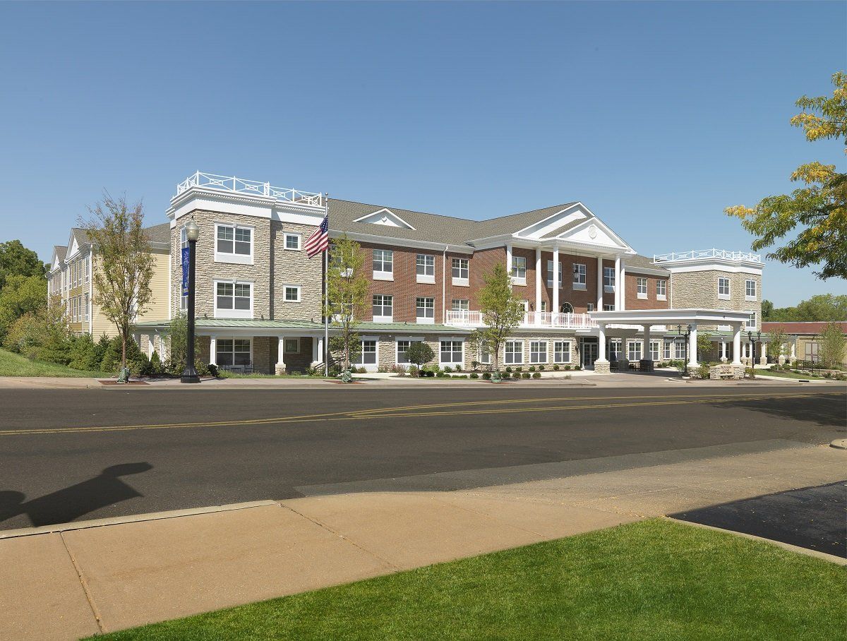 A three-story building with a classical design, featuring white columns and brick details, located alongside a road.