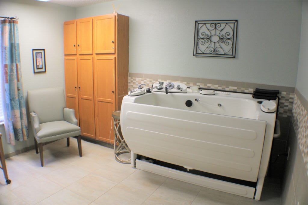 A bathroom featuring a white bathtub, wooden cabinet, and a chair.
