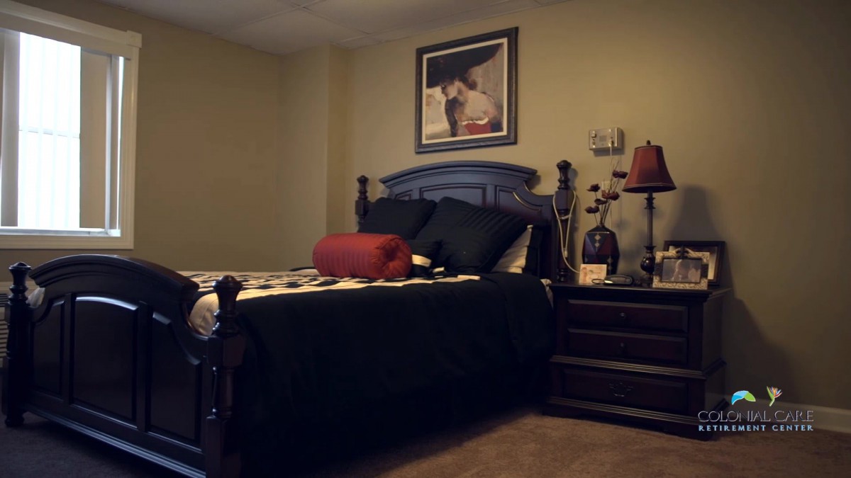 A cozy bedroom with a neatly made bed, decorative pillows, a nightstand with a lamp, and artwork hanging above the headboard.