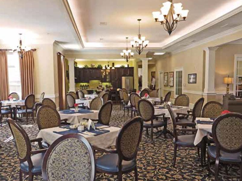 An elegant restaurant dining room with neatly arranged tables and chairs, illuminated by chandeliers.