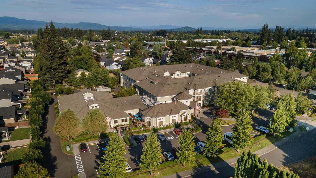 Aerial view of a residential building surrounded by trees and a parking lot in a suburban neighborhood.