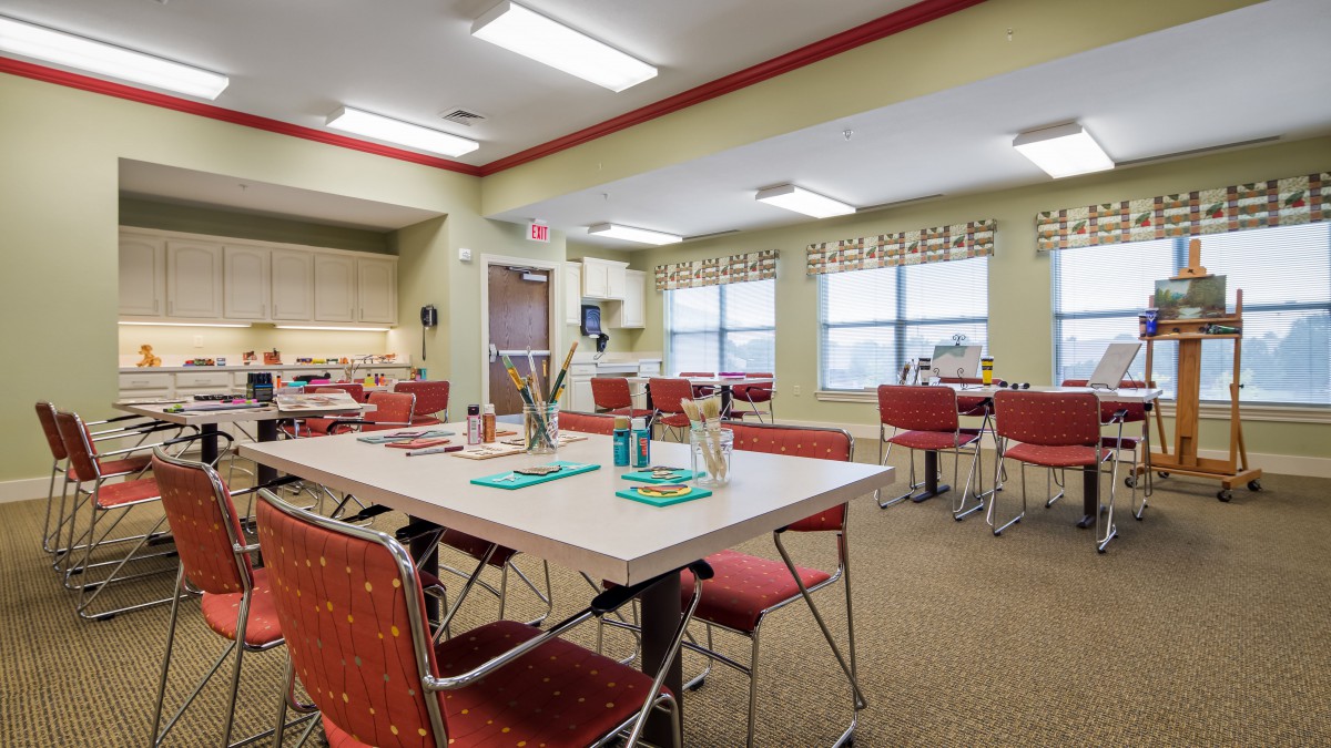 A bright and well-lit dining area with tables and chairs arranged neatly, featuring a small kitchen section.