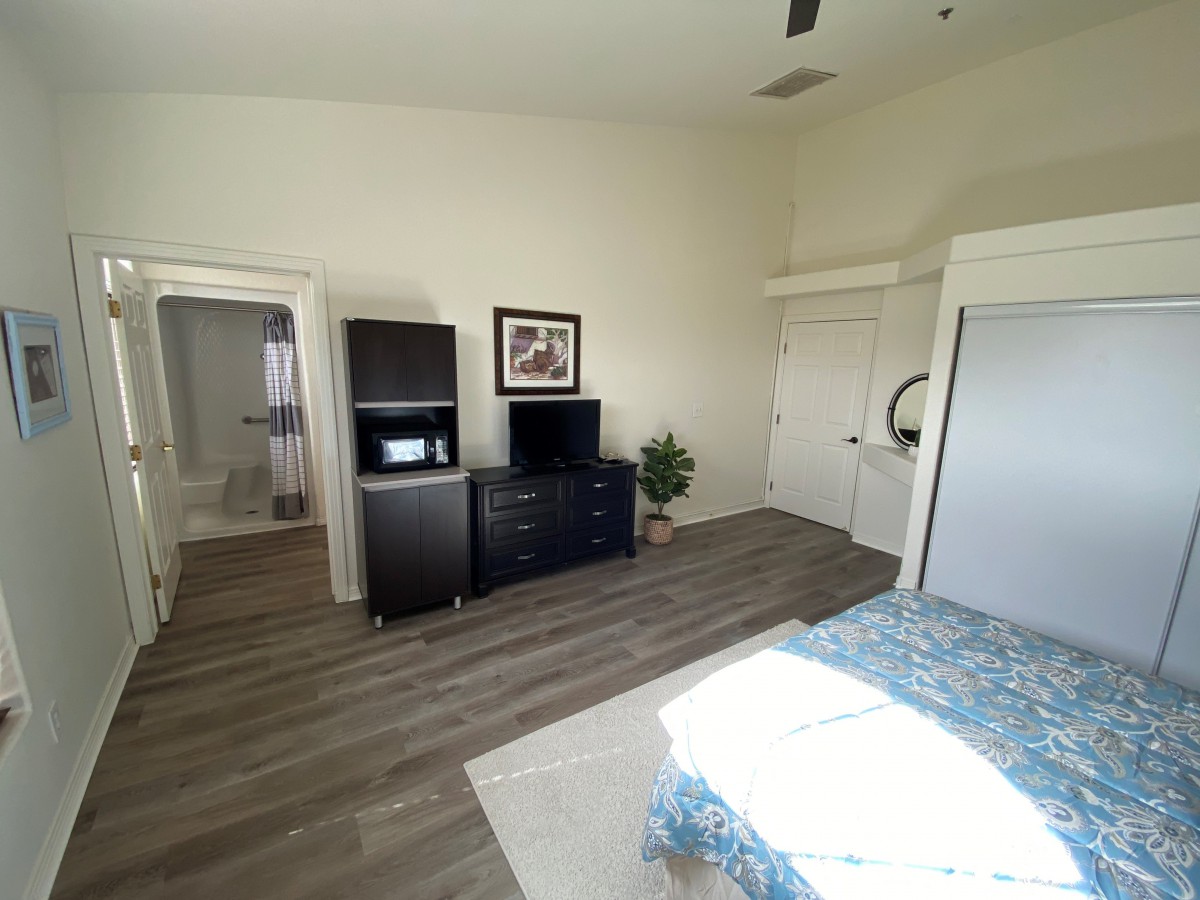 A spacious bedroom with minimalist decor, featuring a dresser, wardrobe, and wooden flooring.