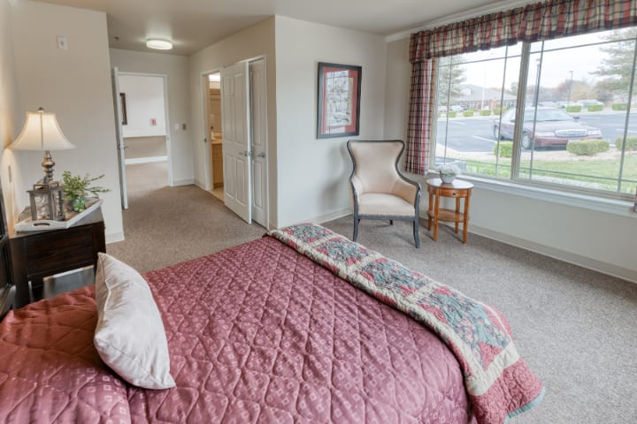 A cozy bedroom with a quilted bedspread, an armchair by the window, and warm, inviting decor.