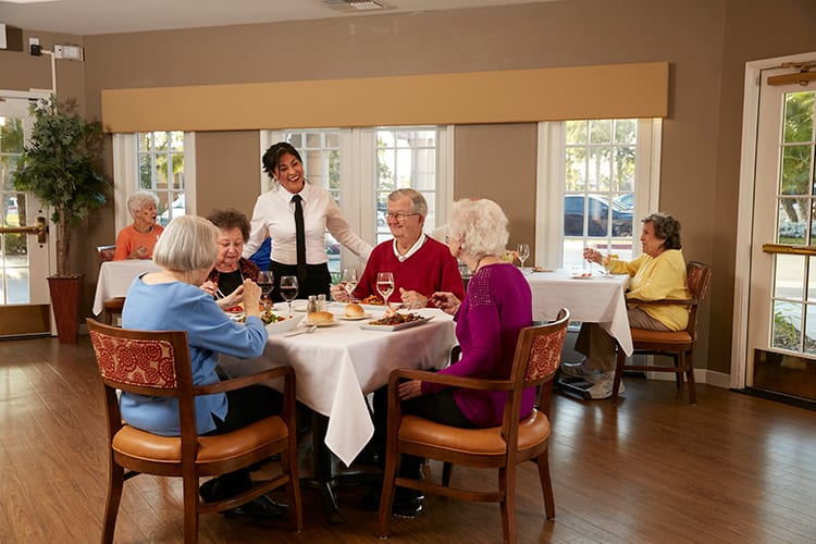 A group of seniors enjoying a meal together in a restaurant with a server attending to their table.