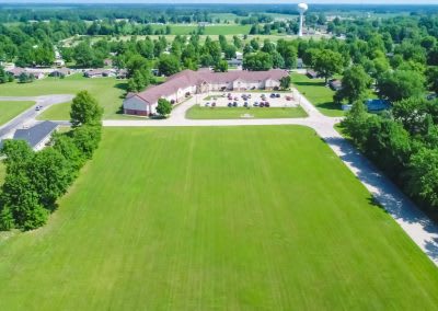 Aerial view of a green field with a building surrounded by trees in a suburban area.