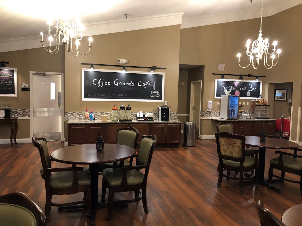 A cozy cafe interior featuring tables, chairs, chandeliers, and a coffee station.
