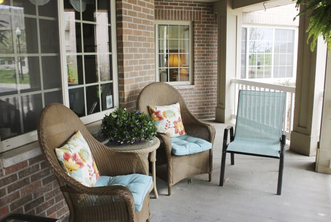 A cozy porch with wicker chairs, a small table, cushions, and a potted plant.